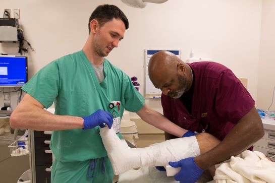 Two medical professionals wrapping person's leg with gauze